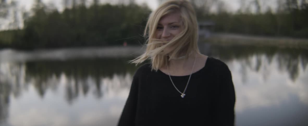 A woman walking towards a lake turns around and smiles in slow motion