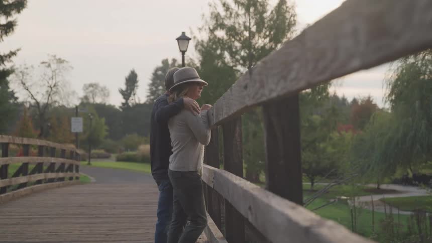 Husband and wife are watching a park trail from a wood bridge