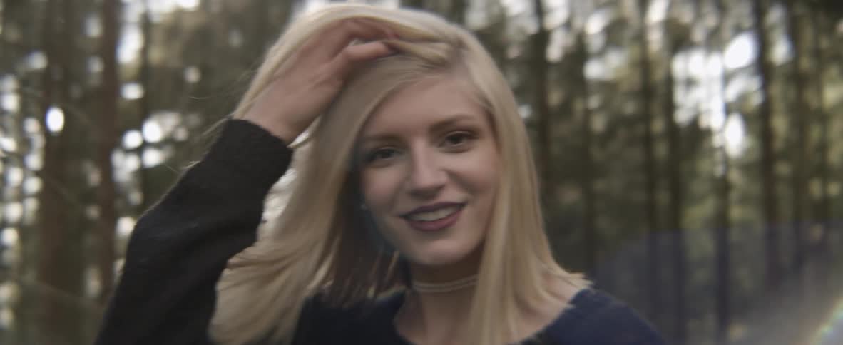 A woman turns brushing her hair and smiling in the forest