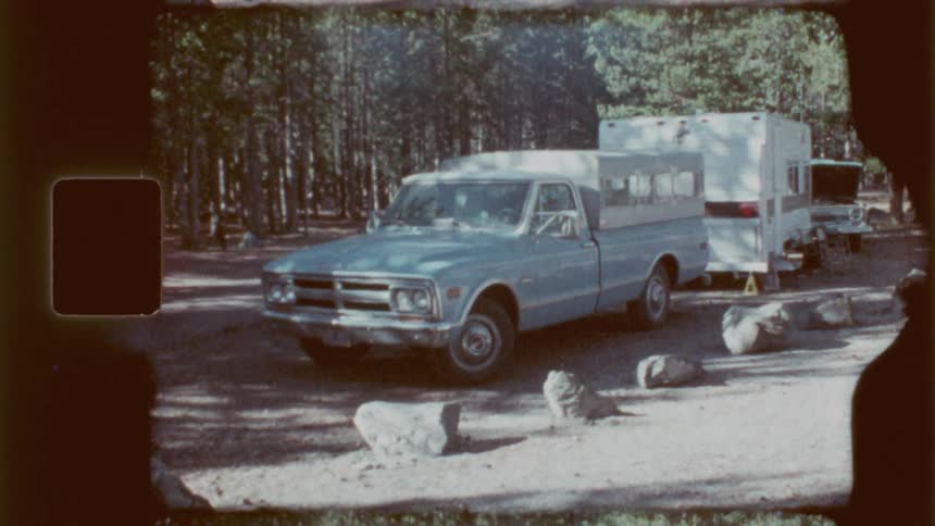A truck hauling a trailer is parked in the forest