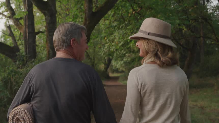 A man and a woman viewed from behind walk together along a path through a wooded area