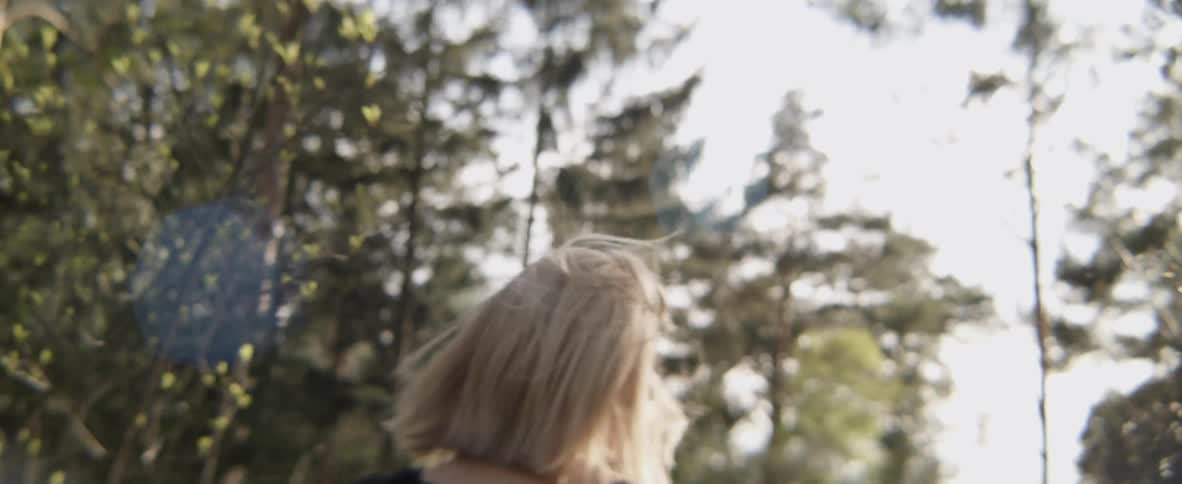 A woman smiles and bounces while walking through a forest
