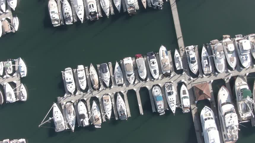 A tilted aerial view reveals rows of boats docked in a marina with the camera pulling back to show more vessels on the water below
