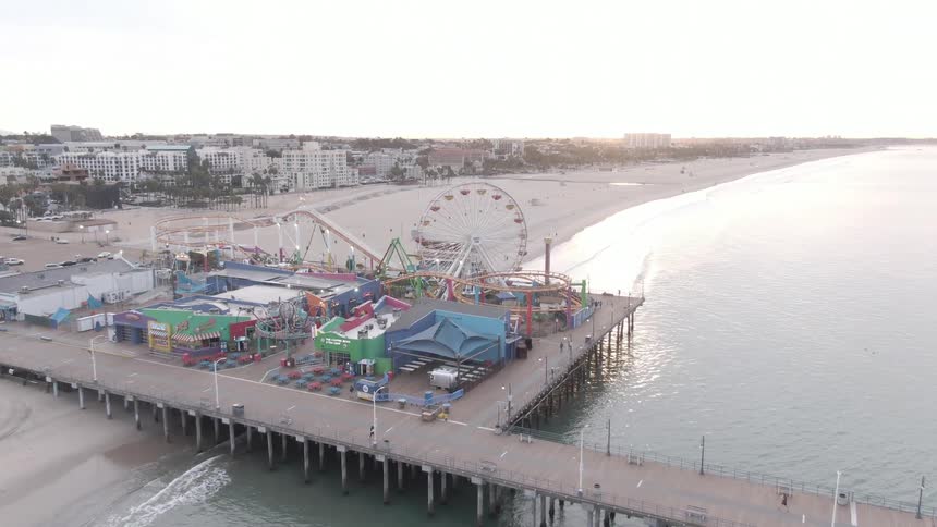 Pedestrians walk on the boardwalk near a carnival located on a beach bordering residential buildings during the daytime