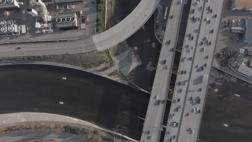 A highway intersection with moderate traffic a river passing underneath the highway and an industrial complex nearby