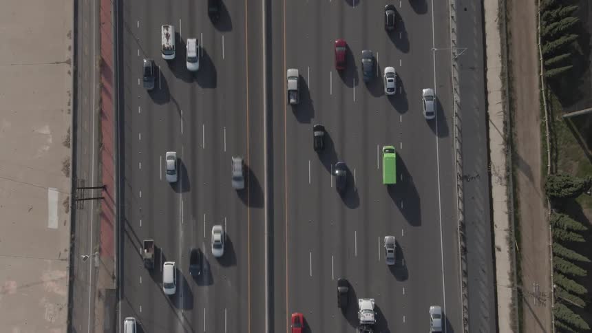 An aerial view shows cars and a truck driving along a multilane highway with a dividing median and concrete barriers