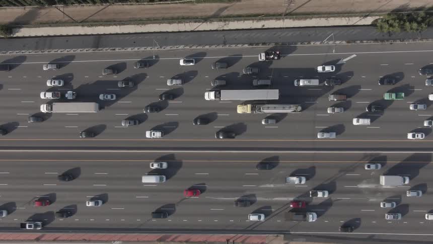 Looking straight down from an aerial perspective heavy freeway traffic includes countless cars alongside large cargo trucks 18wheelers and tanker trucks navigating the multilane highway during the day