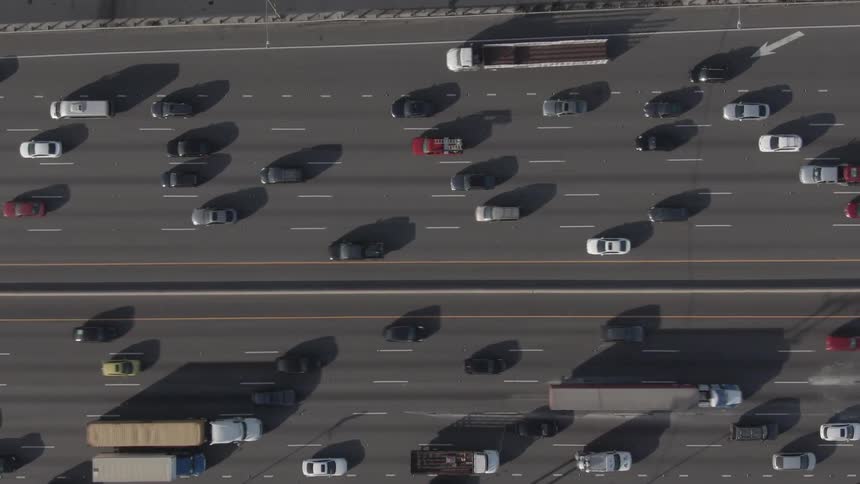 An aerial view of the flow of vehicles along a multilane highway with cars and trucks casting long shadows on the asphalt
