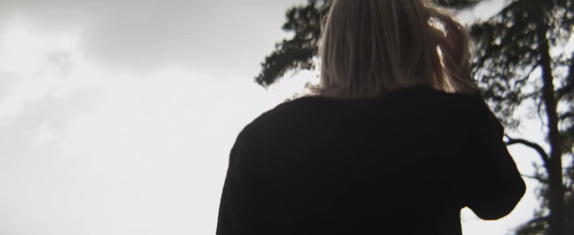 Blonde woman brushing back her hair as she looks toward some trees on a cloudy day