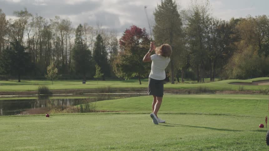 Woman teeing off at golf course surrounded by trees