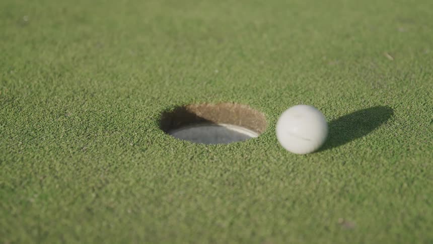Golf ball rolls toward the hole and rolls around the edge