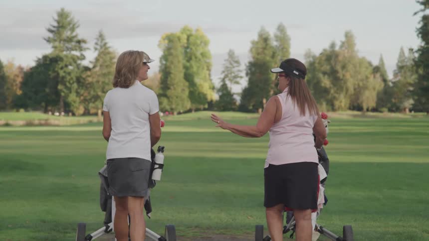 Women push their rolling golf caddies on the grass
