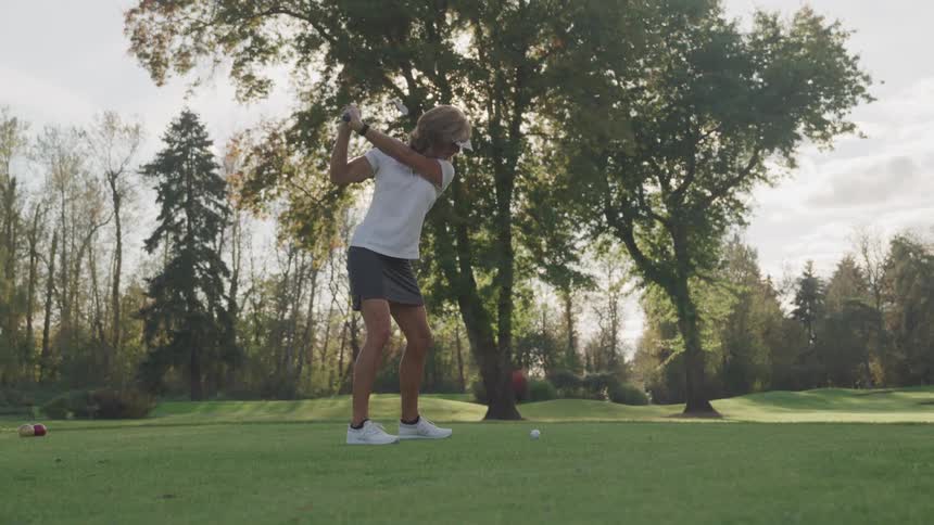 Female golfer swings her club and hits the ball on the golf course