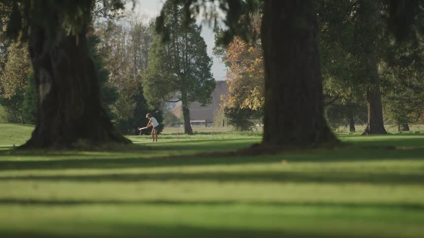 A golfer swings their club on a sunny day surrounded by the lush green grass of a golf course