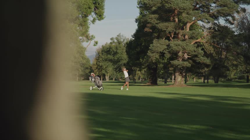 A woman swings her golf club at the golf ball