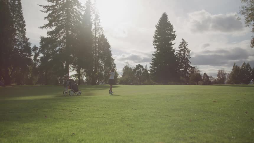 Golfer swings her club and hits the ball across the golf course