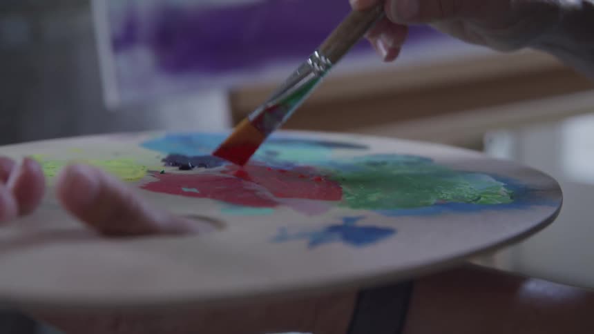 An artist mixes colors on a palette with their paintbrush