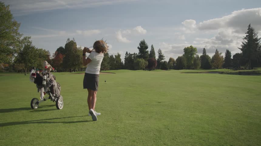 A woman swings her golf club and hits the ball down the green