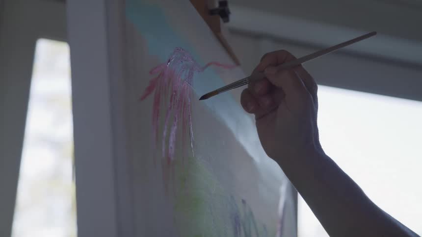 The hand is visible from the right side and is slowly painting a picture on a canvas