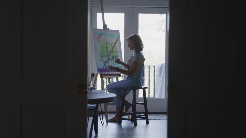 A woman is painting while sitting on a stool