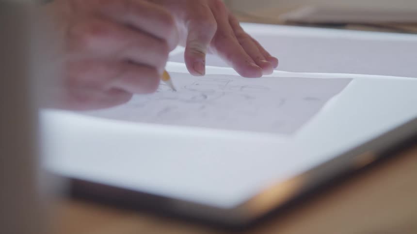 Person uses a light box to trace onto paper with a pencil