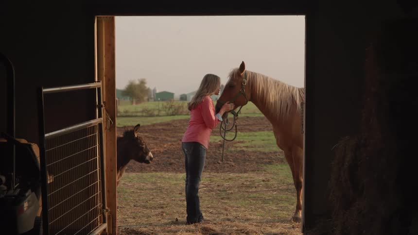 A woman kisses her horse by the barn