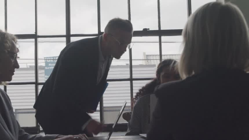 Man in office meeting looking at something on colleagues computer