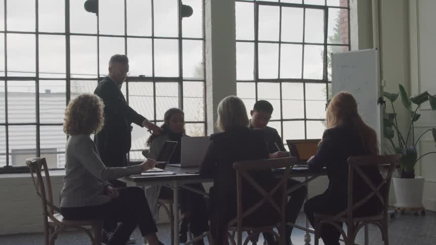 Coworkers in a meeting use their laptops and have a discussion