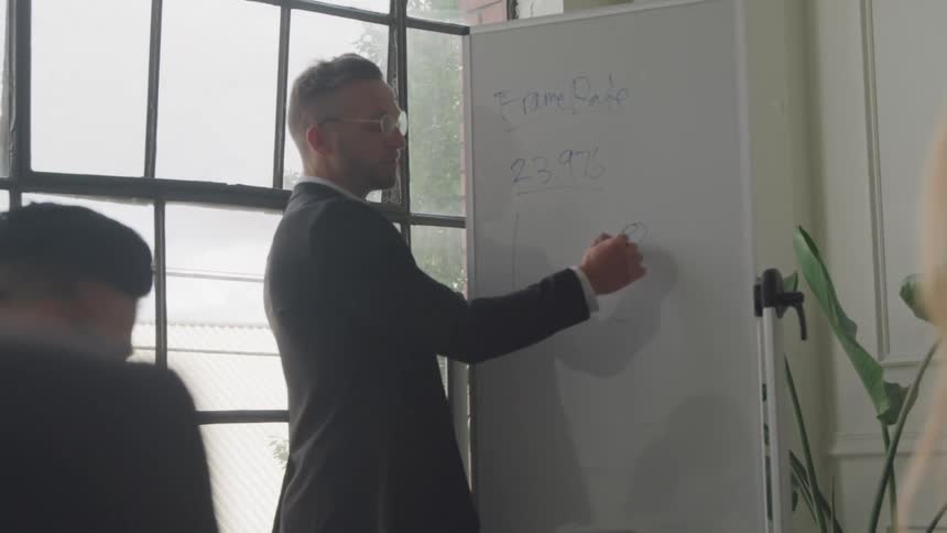 A man is talking and writing on a white board at a meeting