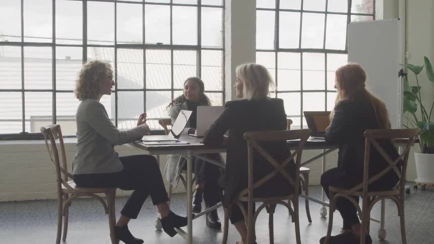 Coworkers sit at a table with their laptops during a meeting at the office