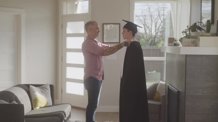 A father adjusts his sons cap and gown and gives him a hug