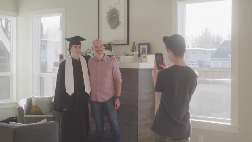 Boy taking photo of father with his son in graduation gown