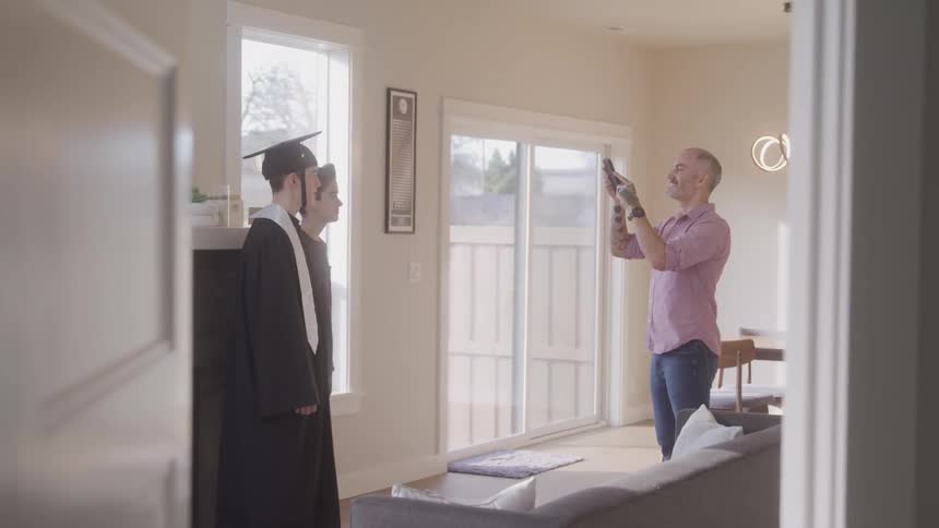 Father takes a picture of a graduate and his younger brother in their living room