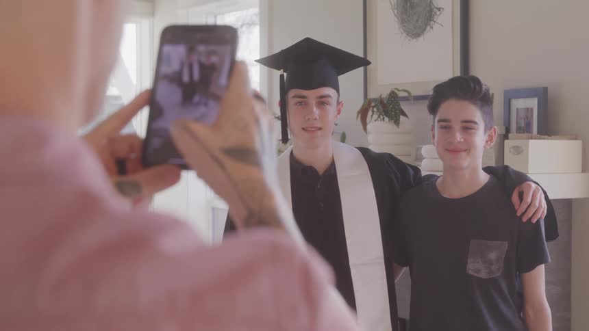 Brothers putting arms around each other as father takes picture on cell phone