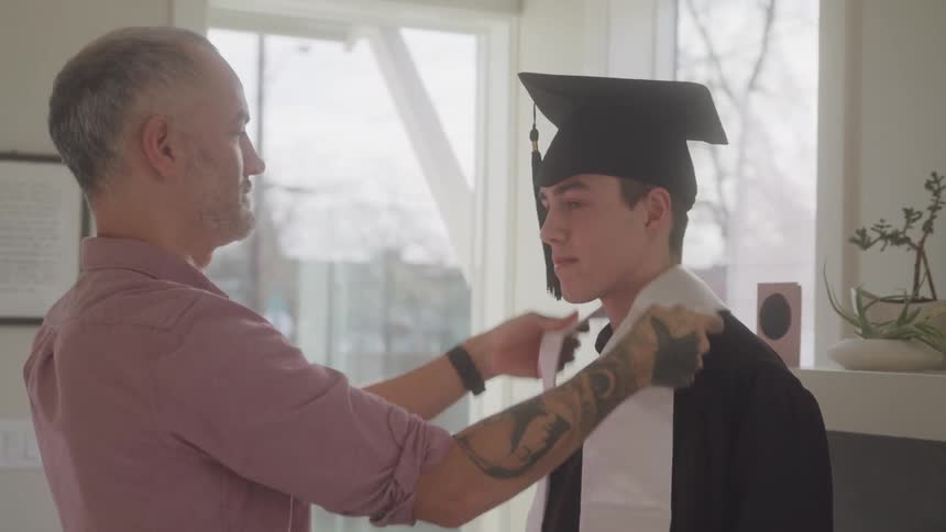Proud father adjusting graduating sons tassle and valedictorian stole in living room