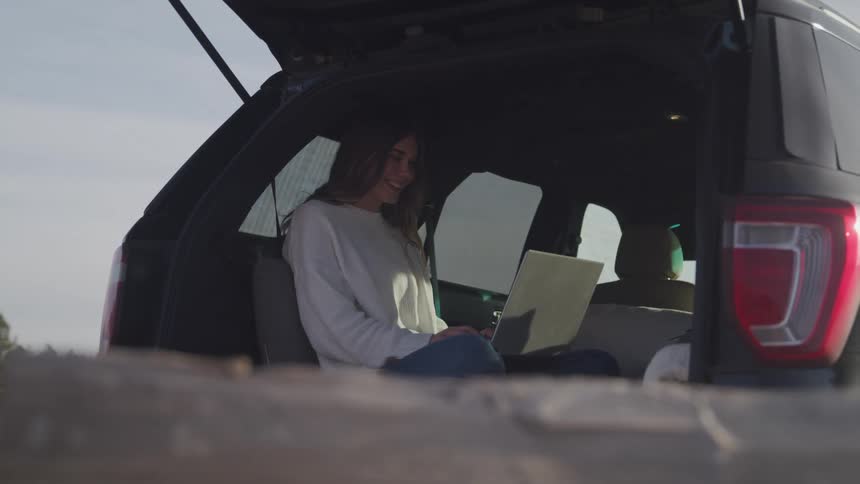 Girl sitting on a car with a computer smiling
