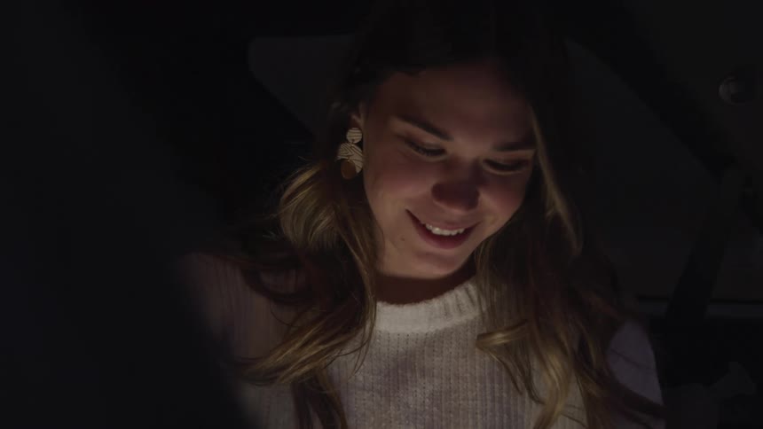 Girl smiles looking at a screen at night