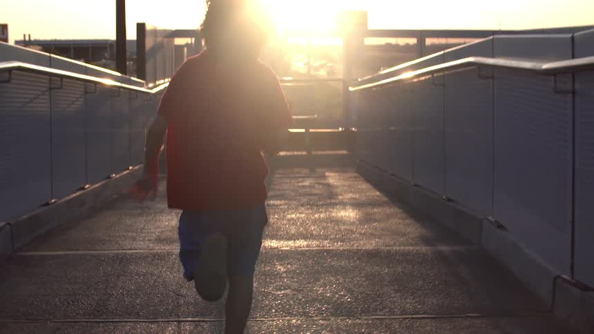 A boy runs on a sidewalk at sunset