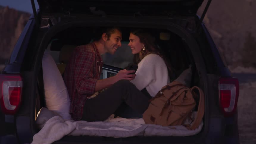 A couple look at their laptop while camping in the car