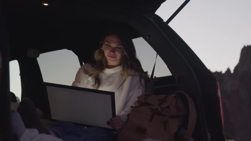 A woman is writing on her tablet in the hatch of her car