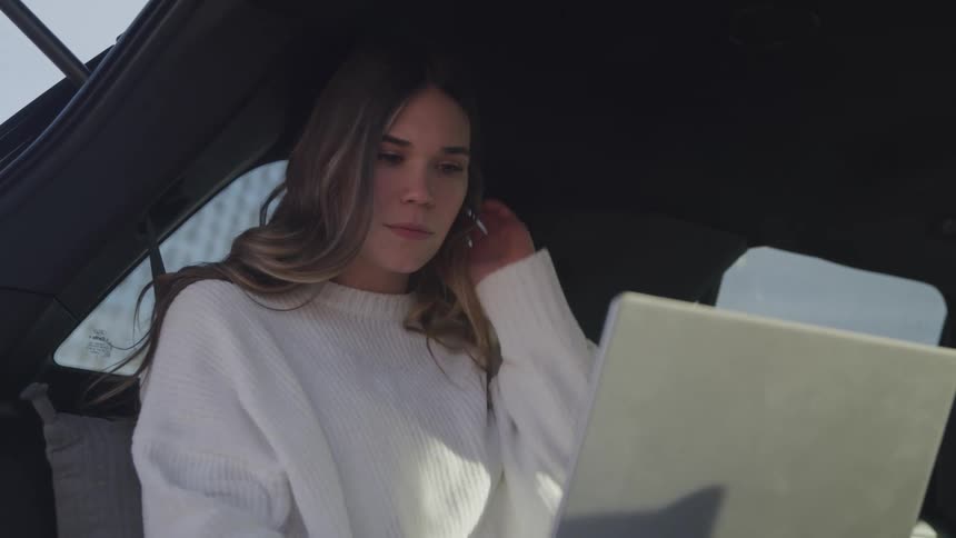 A woman is in a car smiling at laptop
