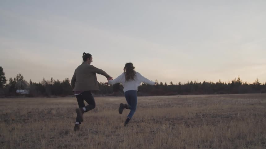 A couple are holding hands and running on the field