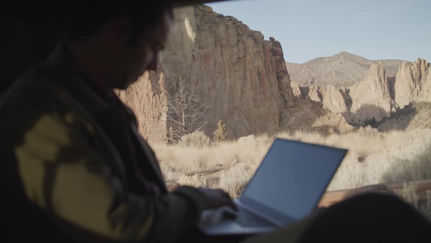 A man who is camping is typing on his laptop
