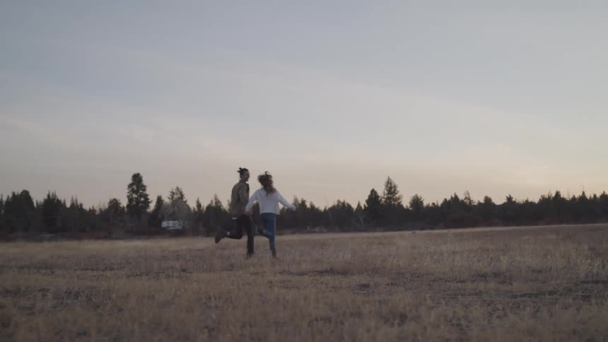 A couple runs through a grassy field holding hands at sunset