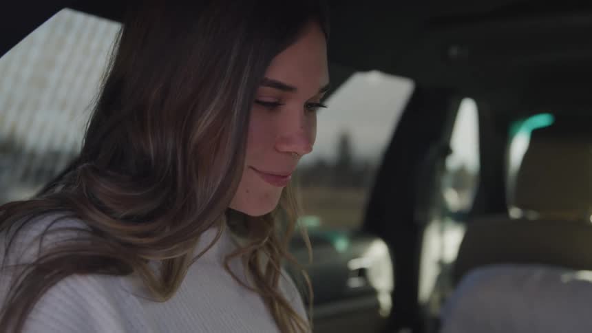 Young woman looks down at someone and smiles while sitting in the back of a car