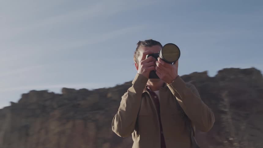 A man uses a camera to take photos against a backdrop of rocky terrain and a clear sky