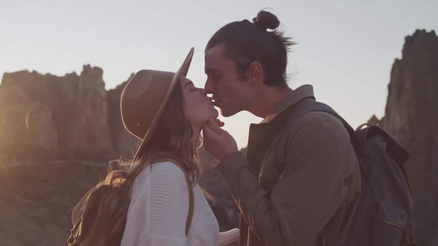 A man and a woman are kissing and the man is holding the womans chin and she is wearing a sun hat