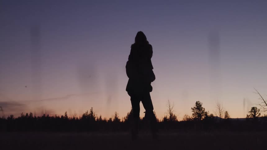 Man holds woman up and spins around at sunset