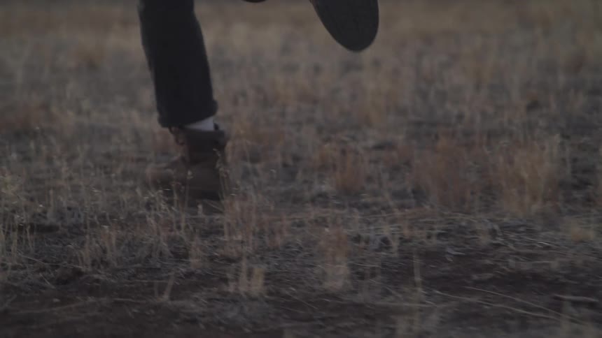 The legs of two people running on a beige grass field