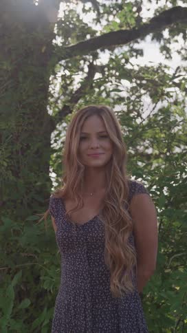 A woman is standing by the tree on a sunny day